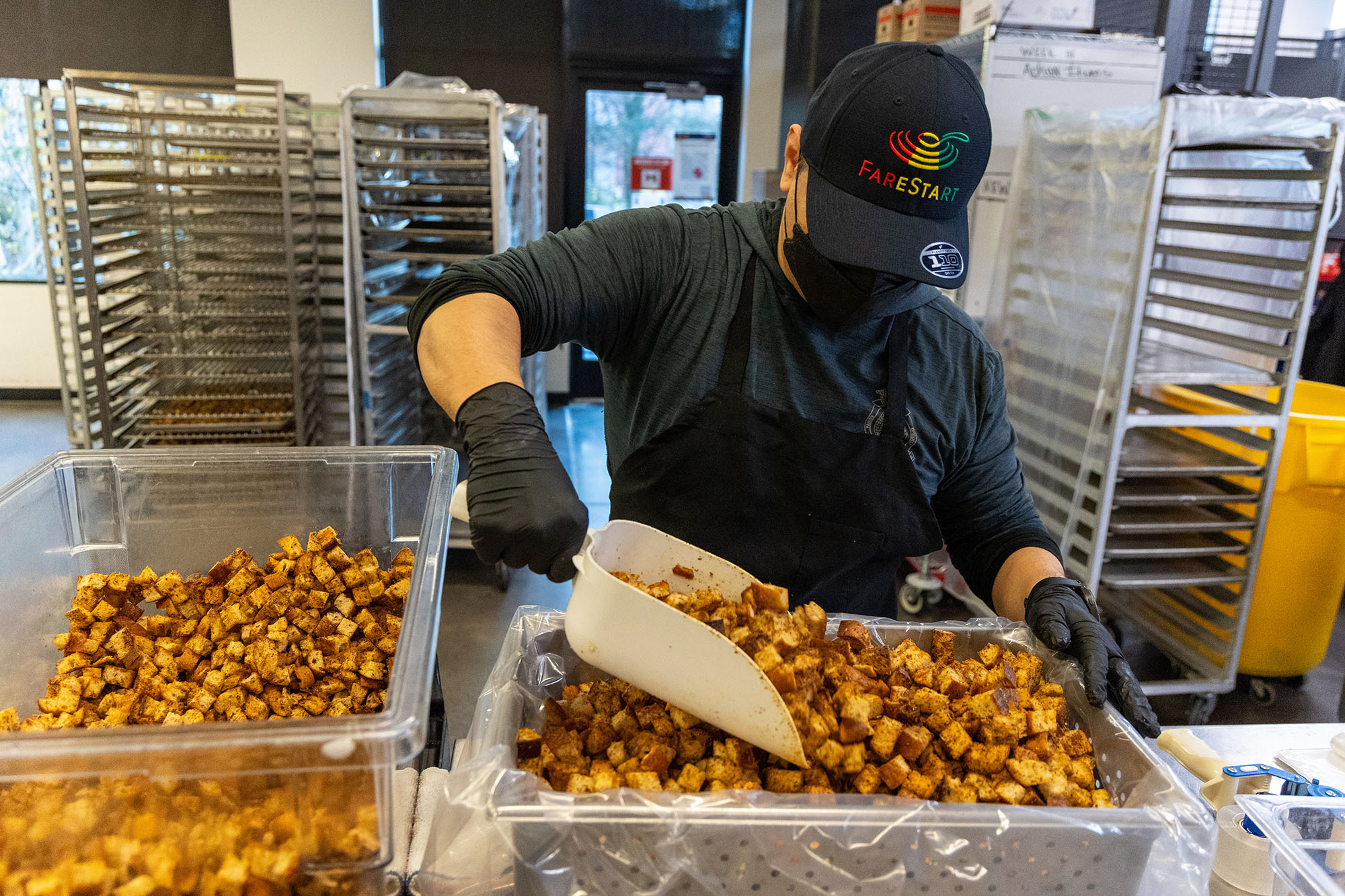 A masked FareStart employee shovels croutons from one container to another. Photo by Meryl Schenker.