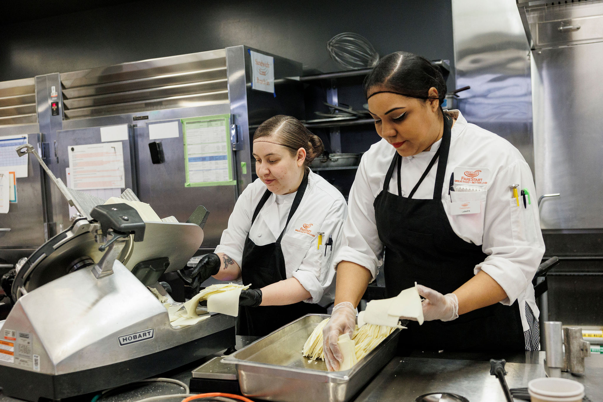 Two Food Pathways Program students slicing cheese with an industrial slicer
