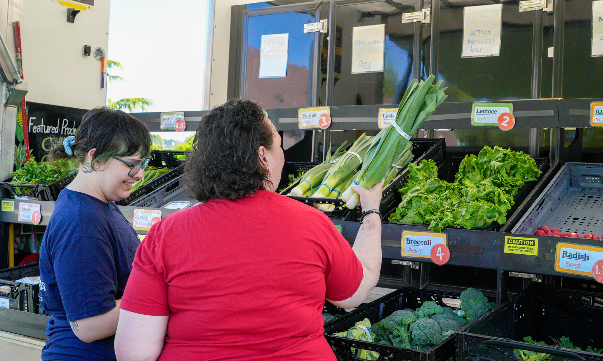 Mobile Community Market customer holding leeks with FareStart staff