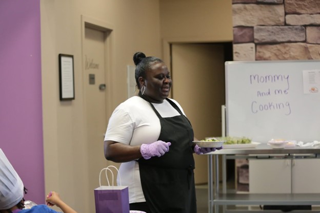 LaTanya, a FareStart graduate wearing a black apron and a white shirt, holding a plate of food.