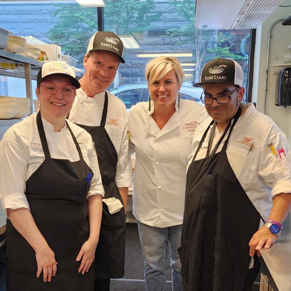 Three FareStart graduates with Chef Kristen Watts Schumacher smiling at the camera