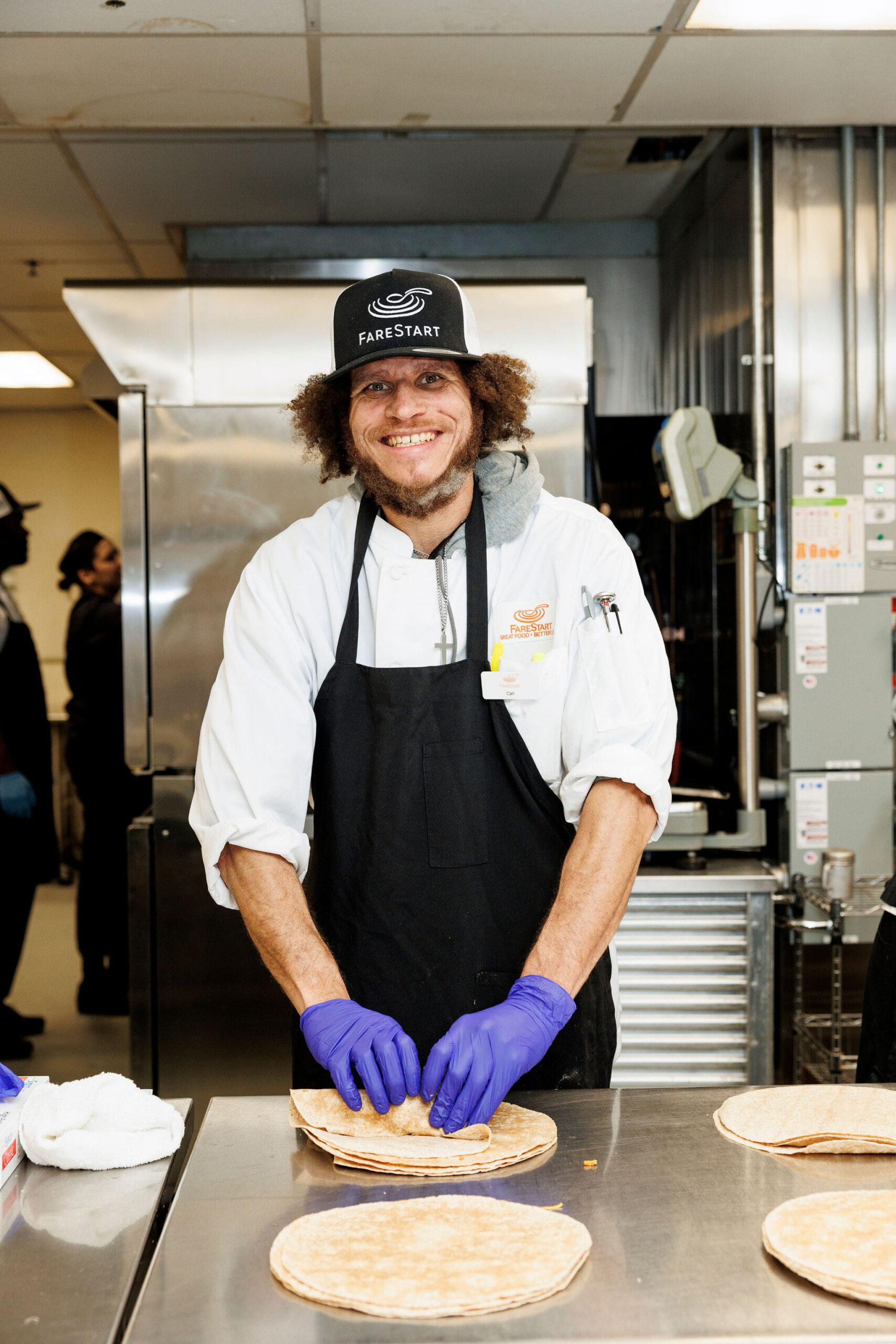A FareStart student folding tortillas in a commercial kitchen smiling at the camera