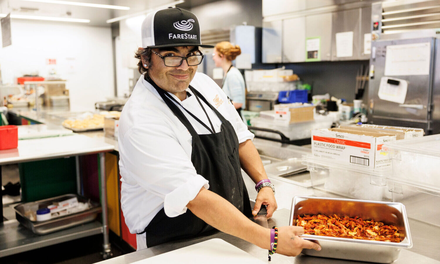 FareStart Graduate, Angel smiling at the camera and holding a pan of peppers