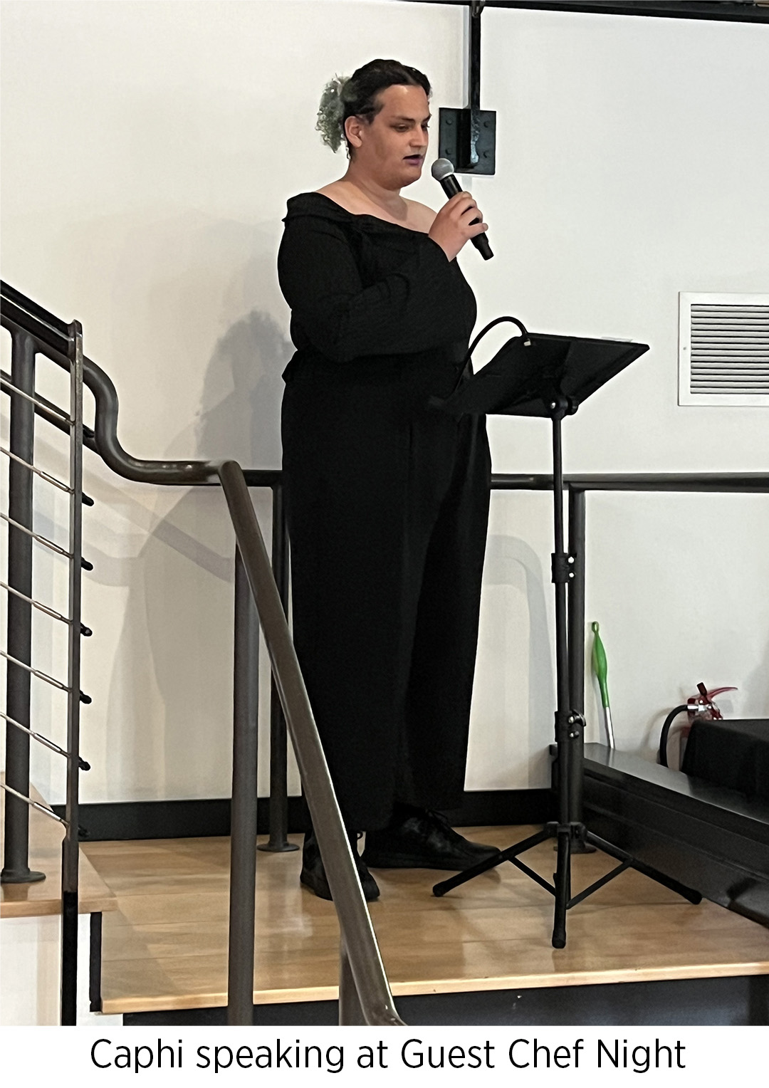 Caphi speaking into a microphone on the staircase in the FareStart Restaurant during Guest Chef Night