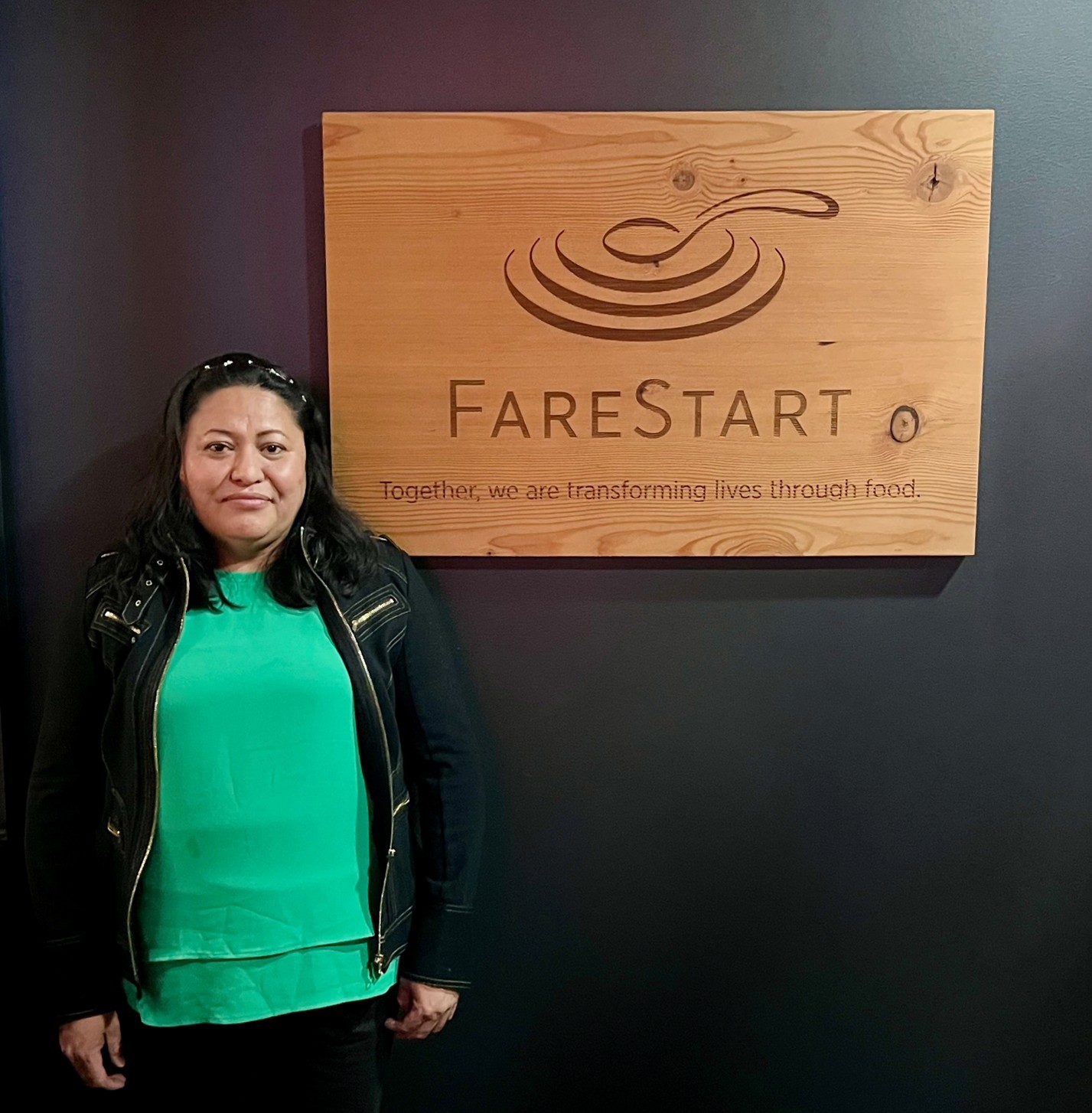 Adriana, a FareStart graduate, posing with the FareStart sign in the FareStart Restaurant