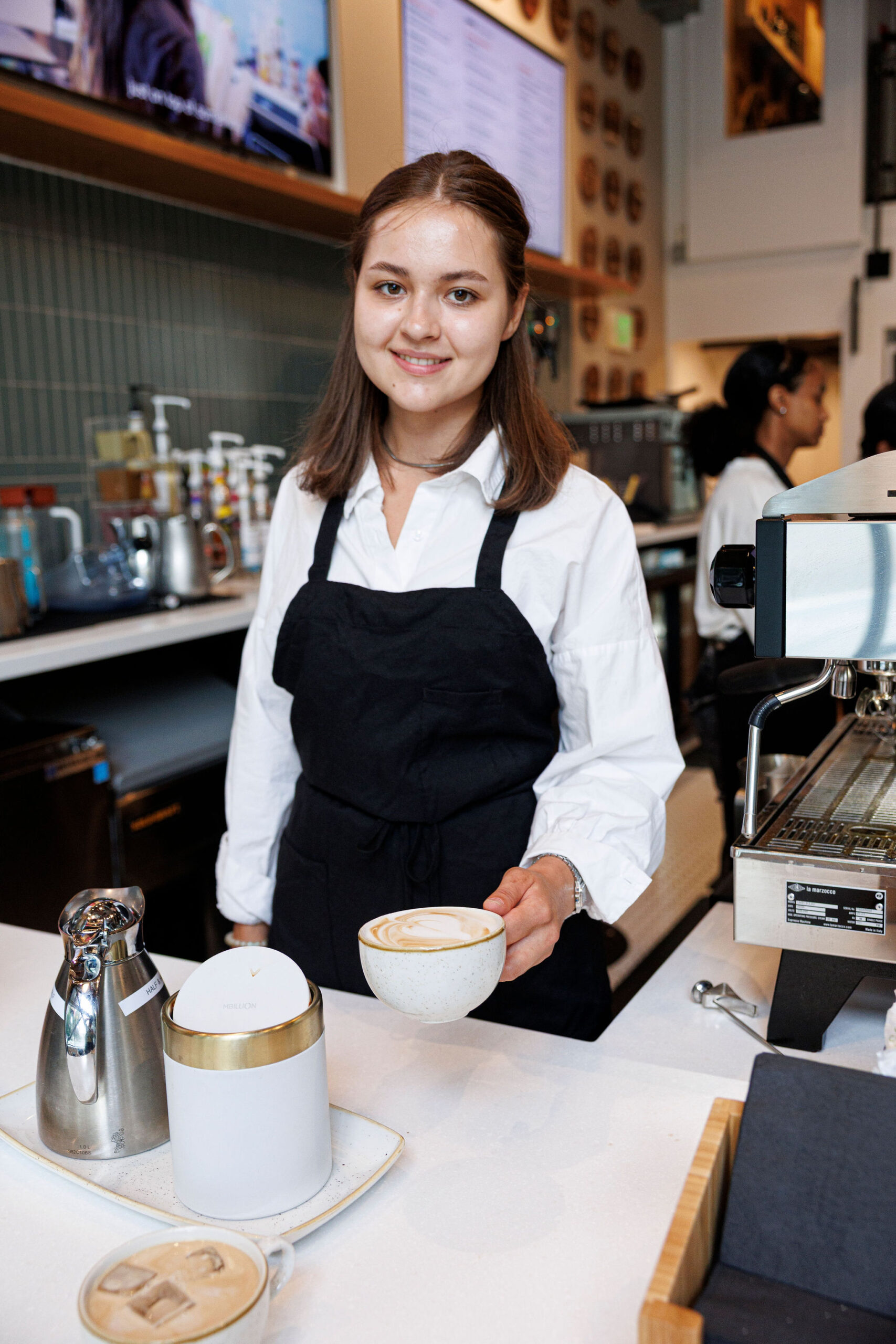 A Barista and Customer Service Student serves a latte with latte art in a cafe setting,