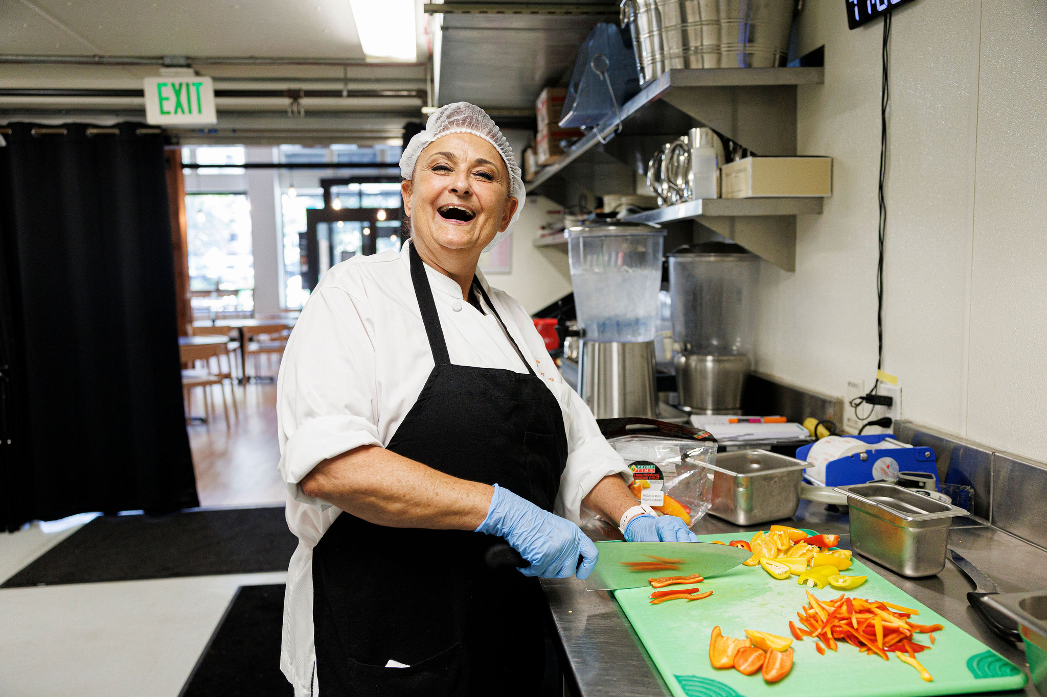 A FareStart student laughs at the camera while chopping peppers in a commercial kitchen setting