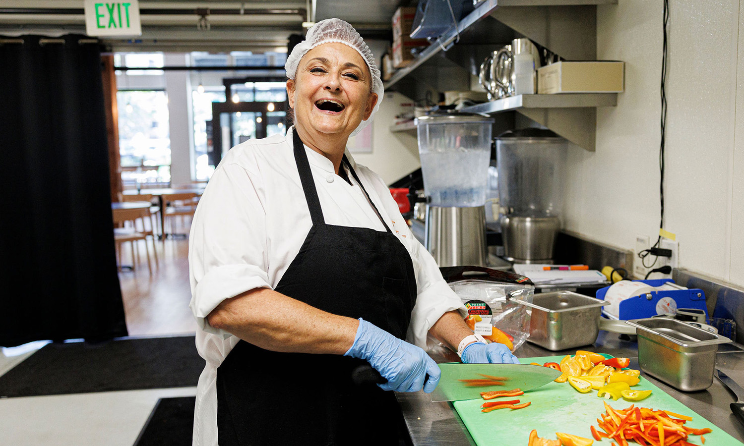 A FareStart student laughing at the camera while chopping peppers in a commercial kitchen setting