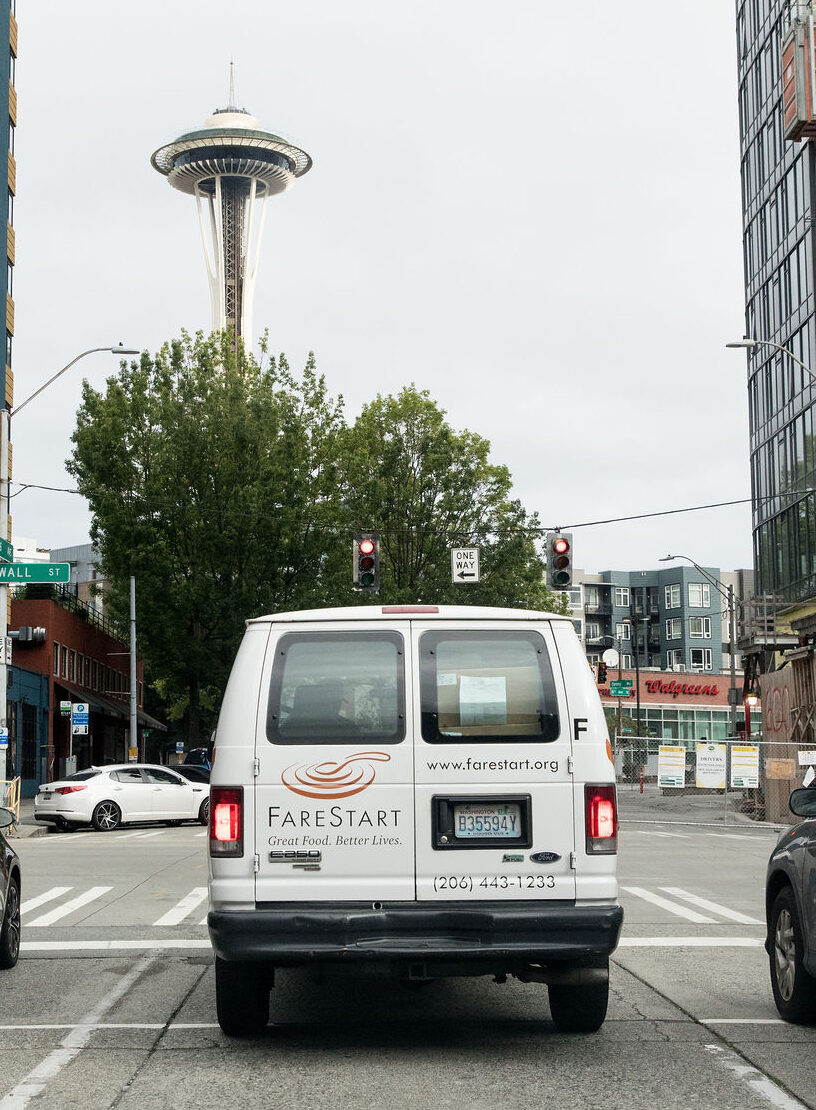 The FareStart delivery van parked in a parking lot. The Space Needle can be seen in the distance