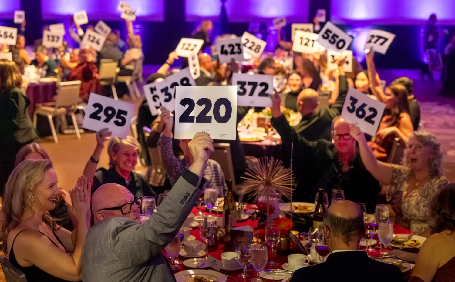 People sitting at a table holding bid cards in the air at FareStart's 33rd Annual Gala Auction & Dinner