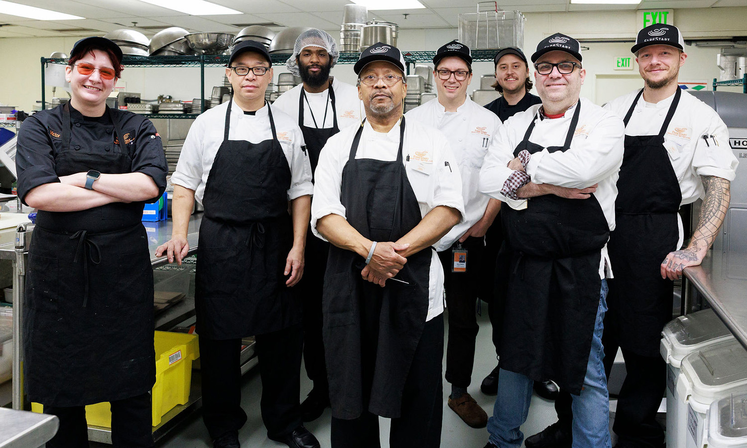 Eight adults (three FareStart chef trainers and five Food Pathways Program students) standing in a group smiling