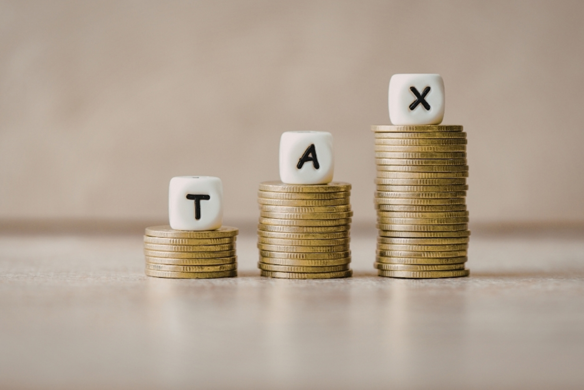 Three dice with the letters "T", "A" and "X" stacked on coins