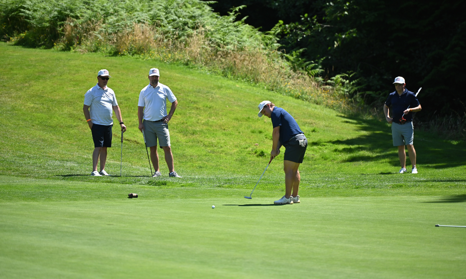 three golfers watching one make a put on the green at the Amazon Golf Tournament